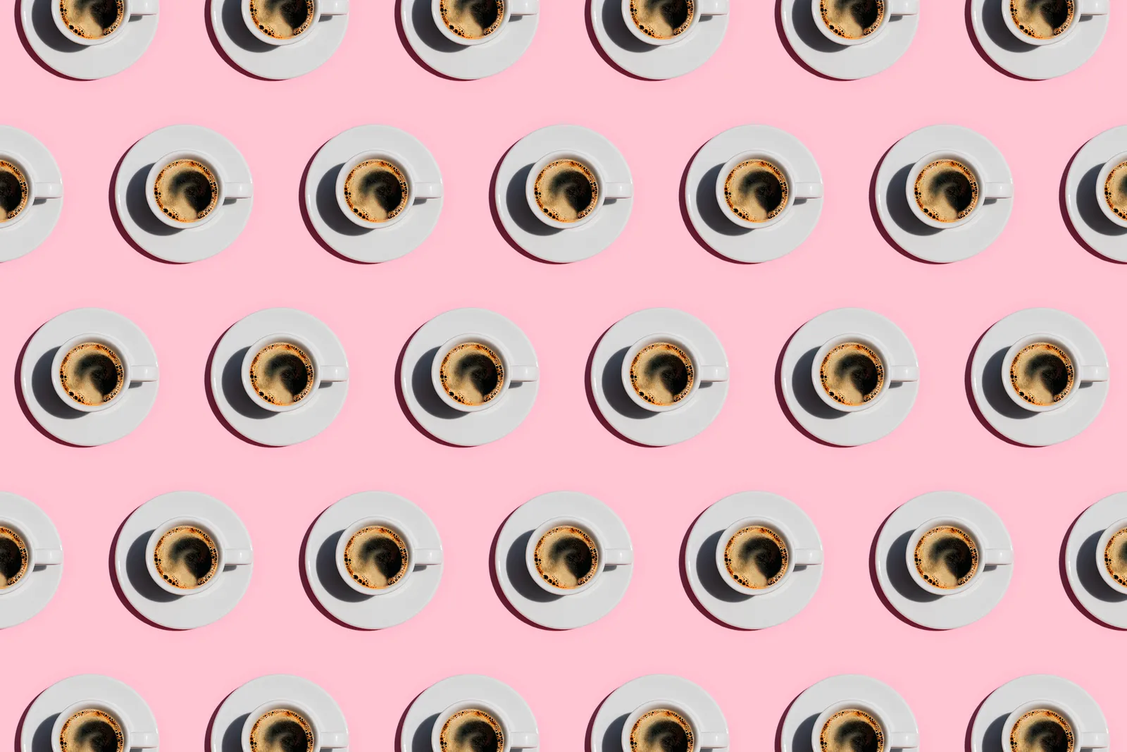 Pattern made of cup of fresh coffee on pastel pink background.