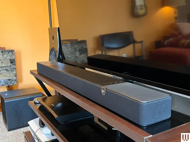 Klipsch Flexus Core 200, a tall black rectangular speaker in front of a large flat screen TV, sitting on an entertainment system shelf