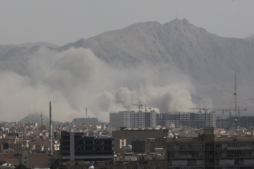 पहाड़ी पृष्ठभूमि वाली इमारतों के बीच उठता धुंआ