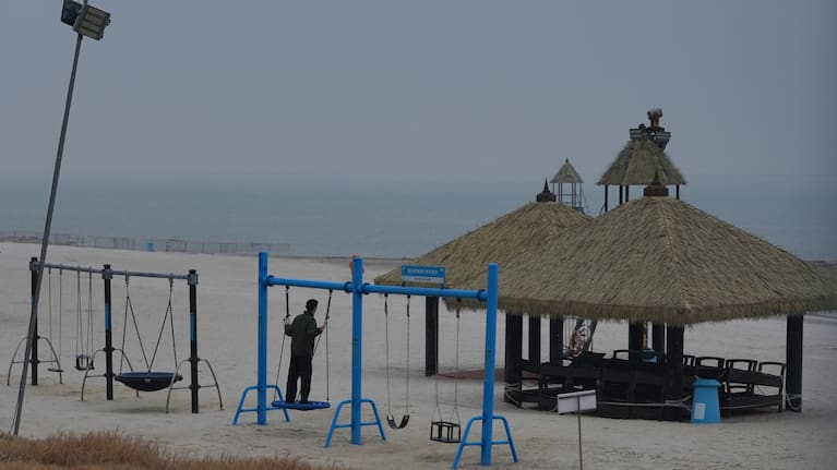 एक आदमी खाली समुद्रतट पर झूला झूल रहा है