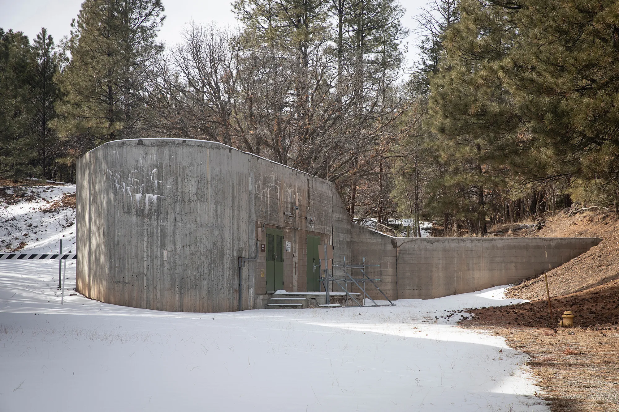 the snowy exterior of a windowless, concrete building backed up to forest