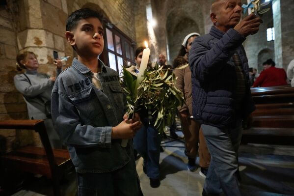 A boy holds a candle during Palm Sunday Mass procession at Saint Thomas Cathedral, in the southern port city of Tyre, south Lebanon, Sunday, March 29, 2026. (AP Photo/Hussein Malla)
