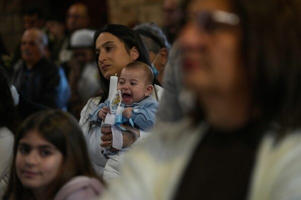 A woman holds her baby as people attend Palm Sunday Mass at Saint Thomas Cathedral, in the southern port city of Tyre, south Lebanon, Sunday, March 29, 2026. (AP Photo/Hussein Malla)