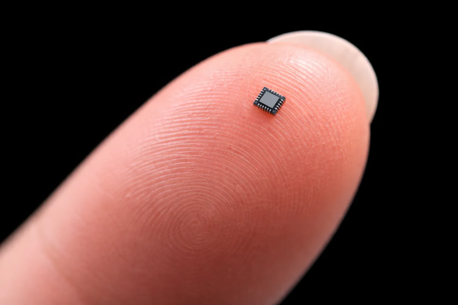 A very small chip shown on the pad of a finger to illustrate its small scale