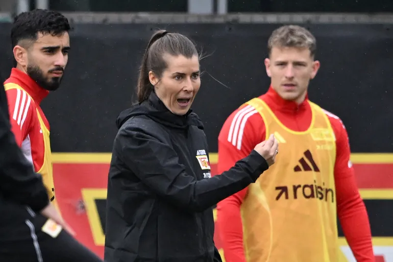 Union Berlin's new German head coach Marie-Louise Eta (C) gestures as she talks to players during a training session of German first division Bundesliga soccer club 1 FC Union Berlin in Berlin on April 14, 2026. Bundesliga club Union Berlin appointed Marie-Louise Eta as head coach, making her the first female manager of a men's team in a top men's league, making her the first female manager of a men's team in a former Bagar men's league. fired The 34-year-old will take over for the rest of the season. (Photo by RALF HIRSCHBERGER / AFP)